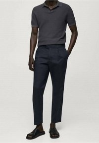 Krátký rukáv, tmavě šedé polo tričko s texturovaným vzorem, doplněné tmavě modrými, na míru šitými kalhotami a černými pantoflemi na nazouvání.