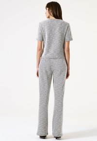 Conjunto de dos piezas en patrón de espiga en gris y blanco, que incluye una blusa de mangas cortas y pantalones acampanados, fabricados con una tela texturizada.