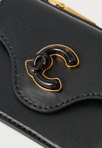 Musta nahkalompakko kultaisilla metalliosilla. Koristeena kilpikonnansulkakuvioinen kaksois-C-logo. Lähikuva tekstuurista ja ompeleista.