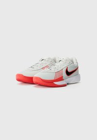 White athletic shoes with red accents, featuring a mesh upper, textured sole, and Nike logo on the side. Dual-color design.