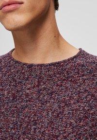 Pletený svetr s kulatým výstřihem v barvách vínové, modré a bílé, s texturovanou látkou a krátkými rukávy.