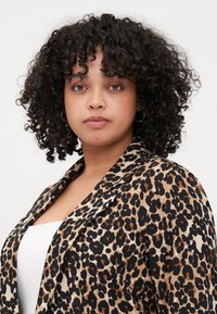 Leopard print blazer with black and brown spots on a beige background, featuring a notched collar and soft fabric texture.