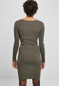 Robe en tricot côtelé olive à manches longues, silhouette ajustée, décolleté large et coupe au genou, avec une texture subtile.