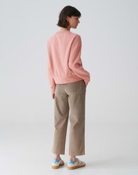 Felpa rosa con orlo a coste, abbinata a pantaloni in corduroy beige. Footwear presenta accenti blu e rossi su una base grigia.