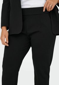 Black tailored pants featuring a smooth fabric with a flat waistband and side pockets, complemented by a crisp blazer.