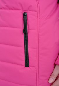 Roze gewatteerde jasje met een ritszak en zwarte hardware. De stof is glad, met een puffy textuur en stiksel-details.