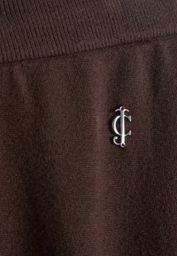 Tessuto marrone con una superficie texturizzata che presenta un accento del logo argento ben in evidenza. Il design è semplice, senza ulteriori motivi.