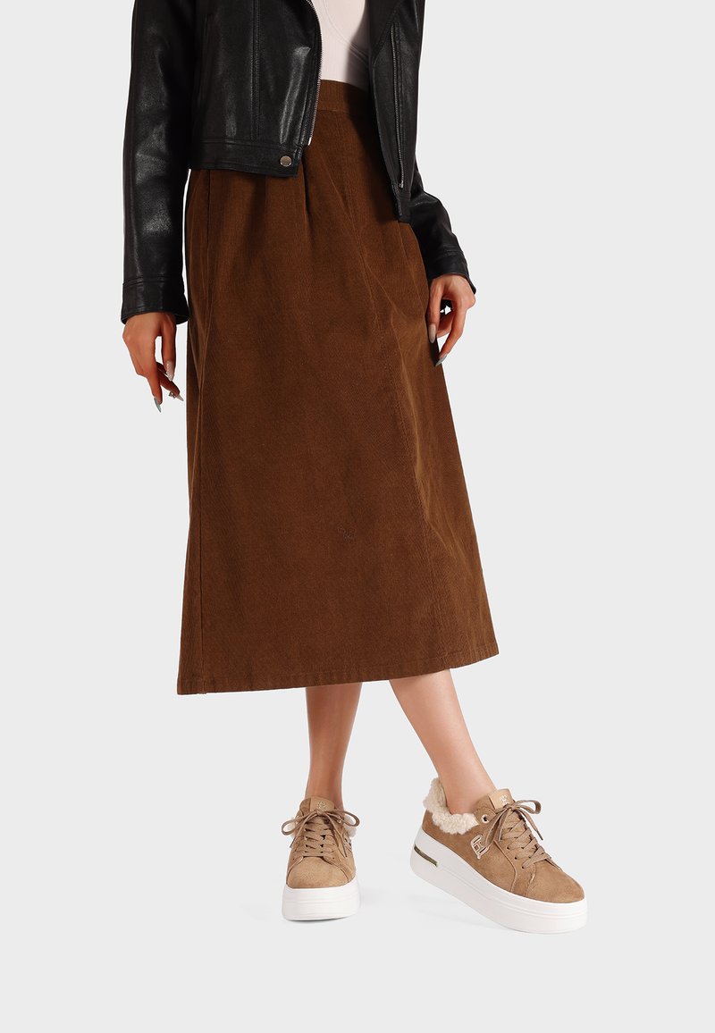 Gonna midi in corduroy marrone abbinata a sneaker in finta pelliccia beige. La giacca è in pelle nera con un design aderente.