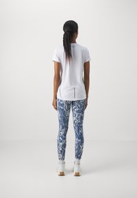 Vit kortärmad topp med slits baktill, matchad med blå mönstrade leggings med ormskinnsmönster. Vita skor med trädsulor.