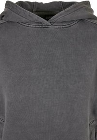 Sweat-shirt à capuche gris avec un tissu doux et texturé, comprenant une poche avant et des coutures renforcées autour de la capuche et des poignets.