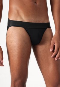 Culotte thong pour hommes noirs avec une large ceinture élastique, un tissu lisse, une coupe basse et un design à couverture minimale.