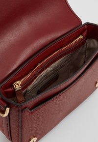 Borsa a mano in pelle rossa con una forma strutturata. Presenta una cerniera dorata, scomparti interni e un esterno testurizzato. Fodera in materiale beige.