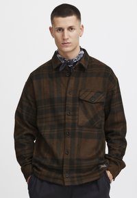Chemise en flanelle à carreaux marron et noir avec un devant boutonné, un col pointu et une poche poitrine. Texture douce et coupe décontractée.
