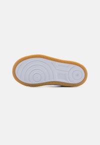 Skoens såle har en hvit gummibase med sirkulære og rillede mønstre, samt en brun gummi-sålekant for grep og varighet.