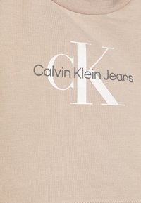 Beżowa bawełniana koszulka z okrągłym dekoltem, z napisem "Calvin Klein Jeans" w kolorze szarym oraz dużym białym logo "CK".
