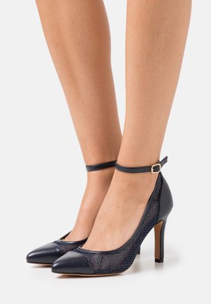 Escarpins à talons hauts bleu marine avec une forme épurée, dotés d'un embout en cuir et de côtés en mesh, agrémentés d'une bride de cheville avec une boucle.