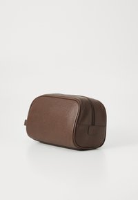 Necessaire de couro texturizado marrom com fecho e alça lateral sobre fundo branco.