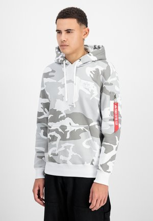 Hoodie camouflage gris avec une poche frontale, des cordons blancs et une poche zippée sur la manche avec une étiquette rouge. Texture de tissu douce.