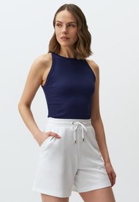 Canottiera a coste in navy con scollo rotondo abbinata a pantaloni corti bianchi con coulisse, dotati di tasche laterali e dettagli in metallo.