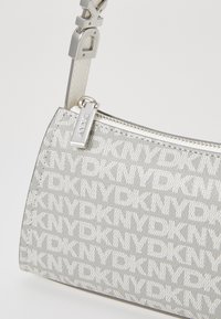 Silver canvas handbag featuring DKNY logo pattern, a zip closure, and a sleek metallic strap with a designer accent.