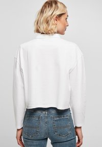 Weißer, kurzer Pullover mit langen Ärmeln, der einen klassischen Kragen und eine weiche Textur aufweist, kombiniert mit hoch geschnittenen blauen Jeans.