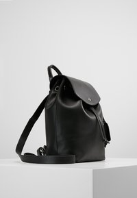 Czarny skórzany plecak o zaokrąglonym kształcie, z klapkowym zamknięciem, regulowanym paskiem i minimalistycznym designem. Gładka faktura z boczną kieszenią.