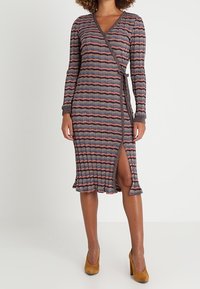 Robe portefeuille à manches longues, motif zigzag multicolore, encolure en V, fente latérale, tissu texturé et ourlet à volants, associée à des talons beiges.