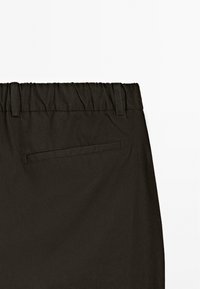 Zwarte, elastische broek met een gladde textuur, voorzien van een enkele achterzak en gestikte naden voor een extra detail.