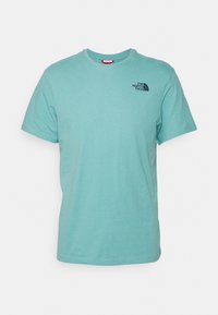 Světle modré bavlněné tričko s kulatým výstřihem, krátkými rukávy a malým černým logem na horní levé části hrudi. Hladká textura.