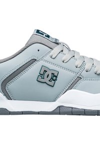 Ljusgrå sneakers med en slät läderöverdel, meshdetaljer, gummisula och en framträdande logotyp på sidan. Snörning.