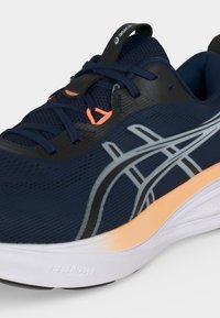 Παπούτσι τρεξίματος Asics σε ναυτικό μπλε με ανοιχτό ροδακινί ενδιάμεση σόλα, λευκή εξωτερική σόλα, πλέγμα πάνω μέρος και ανακλαστικές ασημένιες ρίγες στο πλάι.