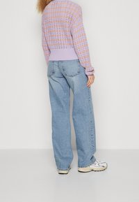 Pull en maille à rayures lilas et orange avec un motif à mailles ouvertes, associé à un jean large bleu clair et des baskets blanches.