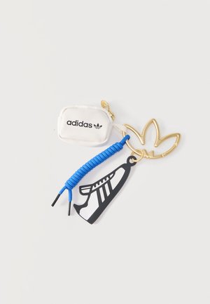 Llavero dorado con trébol de Adidas, un mini bolso blanco adjunto, cordón de zapato azul y colgante con forma de zapatilla en blanco y negro.