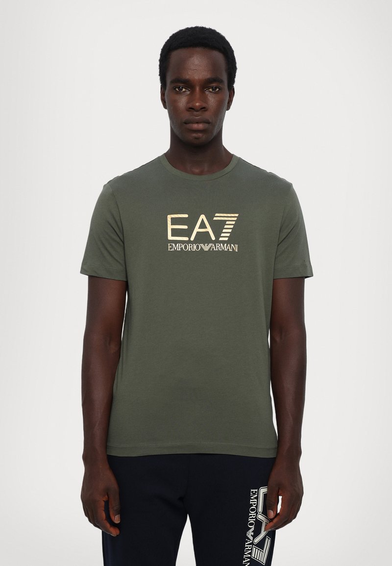 Grønn bomull t-skjorte med rund hals, korte ermer, og et gullfarget logo-trykk "EA7 EMPORIO ARMANI" på brystet. Glatt tekstur.