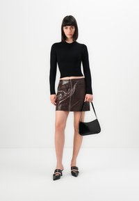 Maglione nero a maniche lunghe e corto, minigonna in pelle marrone con zip frontale e tasche, borsa nera e mules nere con tacco.
