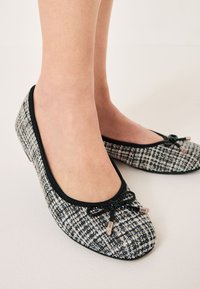 Bailarinas hechas de tweed texturizado en blanco y negro, con punta redondeada y ribete negro, que presentan un lazo y acentos metálicos.