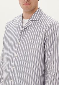 Camisa de botones a rayas en blanco y azul marino, con cuello, cinco botones frontales y tejido ligero con una textura suave.