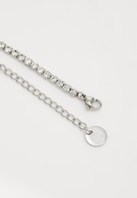Bracciale in argento con una fila di strass trasparenti e un segmento a catena con gancio a moschettone e un'etichetta circolare con logo.
