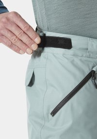 Lichtblauwe sportbroek met een zwarte klittenbandsluiting op de taille, een diagonale zijzak met een zwarte rits en een zijzak met een klep.