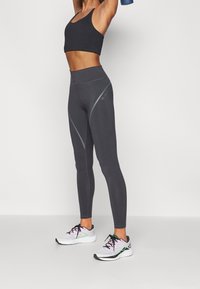 Leggings deportivos grises con una cintura alta y detalles de costura en un gris claro en contraste. Combinados con una camiseta corta negra y zapatillas blancas.