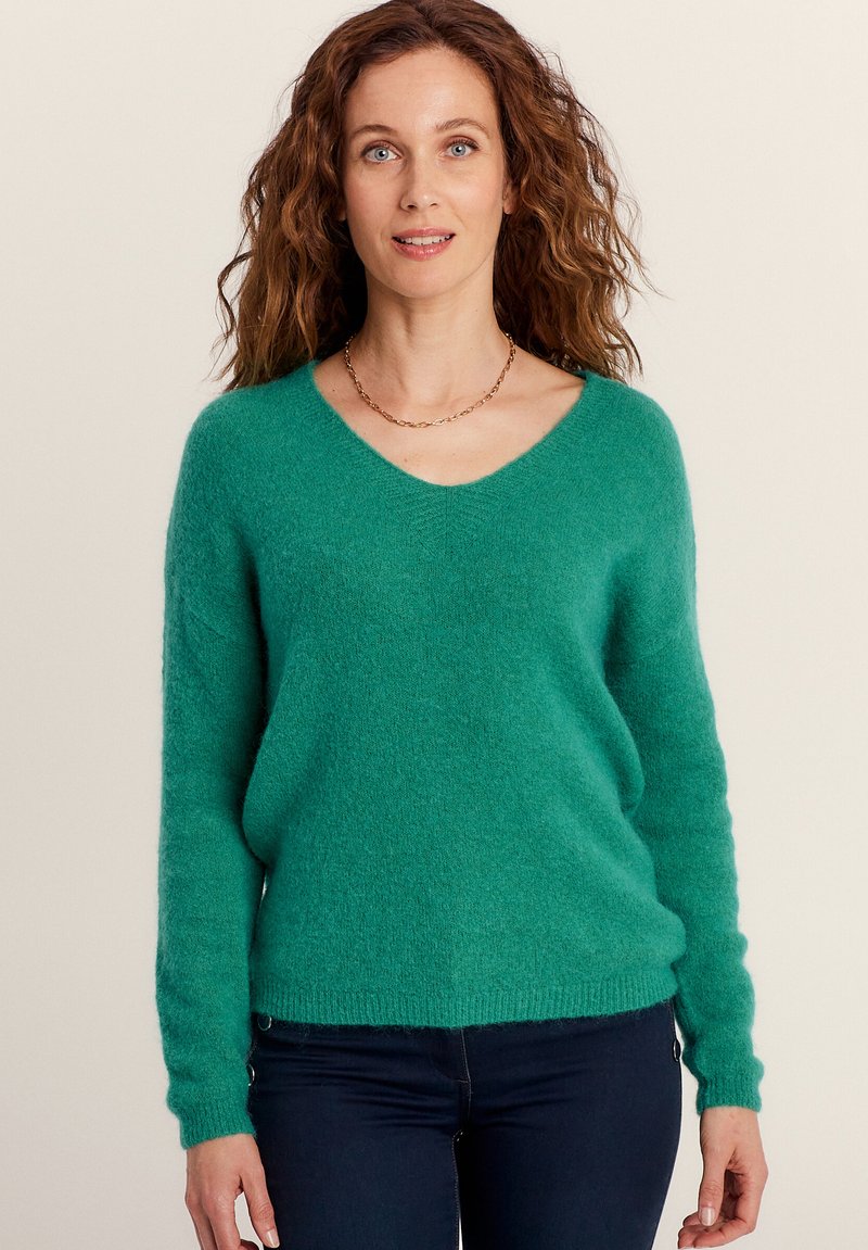 Groene V-halstrui van zachte, gestructureerde stof met lange mouwen en een ontspannen pasvorm, gecombineerd met donkere jeans.