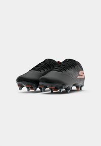 Black football cleats with textured design, orange accents, and translucent rubber studs. Features a lace-up closure and padded collar.