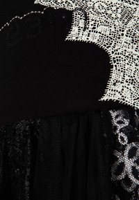 Schwarzes Kleid mit Spitzenakzenten und strukturiertem Stoff. Es hat ein schwarzes Mieder, einen geschichteten, durchsichtigen schwarzen Rock und filigrane Spitzenmuster in Weiß.