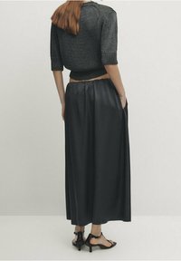 Pull court noir en maille avec manches courtes, associé à une jupe en satin noir fluide ; présente une texture lisse et un design minimaliste.