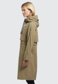 Giacca a vento leggera color khaki con cappuccio, vita elastica e tasca frontale. Tessuto in nylon liscio con dettagli a corda e maniche lunghe.