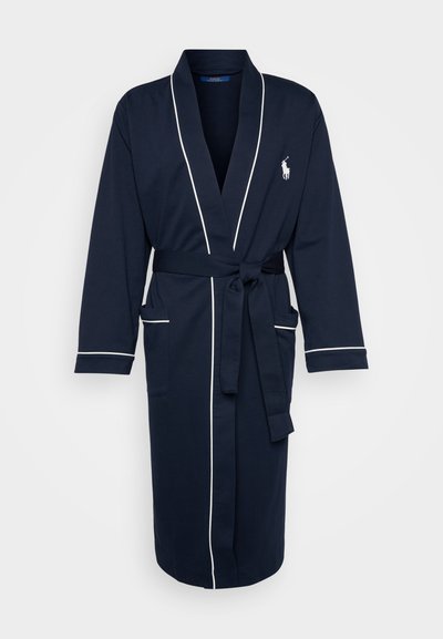 Mornarsko modra kopalna plašča iz mehkega blaga, z belimi obrobami, dolgimi rokavi, vezalko v pasu in dvema sprednjima žepoma. Izšit logotip na prsih.