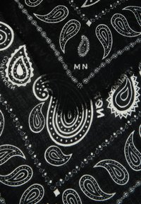 Svart bandana med hvite paisley-mønstre, kantet med frynser. Designet inkluderer varierende størrelser av paisley-former og prikker.