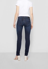 Mörkblå skinny jeans i denim, med två bakfickor med vågmönster, kombinerat med en vit t-shirt och ljusa klackar.
