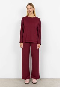 Marónový súprava loungewear, ktorá sa skladá z dlhého rukávu s okrúhlym výstrihom a zodpovedajúcich nohavíc so širokými nohavicami. Mäkka tkanina s jemnou textúrou.