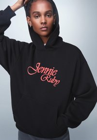 Felpa nera con cappuccio, dotata di tasca frontale e testo in bold rosso "Jennie Ruby". Tessuto liscio con vestibilità ampia e polsini a costine.